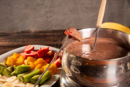 Foto de Fondue de chocolate acompañada de frutas tropicales sobre mesa de madera y fondo oscuro - Imagen libre de derechos