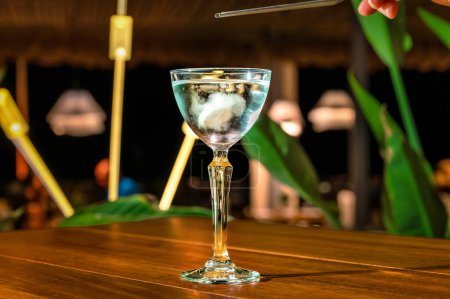 Foto de Concepto de restaurante y bar. Mesa con un vaso de alcohol alto y elegante lleno de bebida azul y hielo, exudando un ambiente elegante y lujoso. - Imagen libre de derechos
