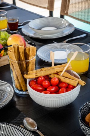 Foto de Close-Up Meal Concept: Table Set for Dining with Cherry Tomatoes, Dried Breadsticks, and Orange Juice (en inglés). Ideal para su uso en blogs de alimentos, publicaciones de estilo de vida y materiales promocionales. - Imagen libre de derechos