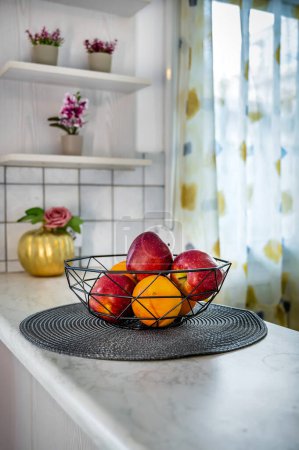 Téléchargez les photos : Concept de cuisine : Bol en métal avec des oranges fraîches et des pommes. Fruits vibrants et colorés disposés dans un bol en métal moderne, créant un point focal dans un décor de cuisine doucement flou. - en image libre de droit