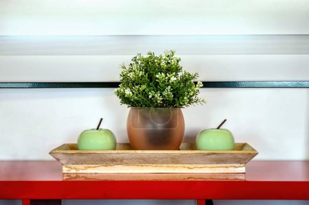 Faszinierende Nahaufnahme eines hölzernen Tabletts mit einer lebendigen grünen Pflanze in der Mitte, umgeben von saftig grünen Äpfeln, die symmetrisch auf jeder Seite platziert sind. Innenarchitektur