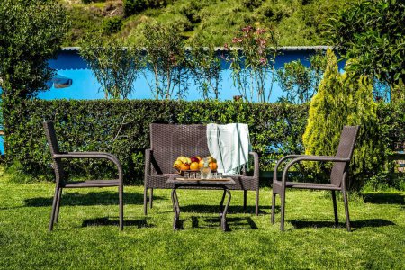 Entspannungsbereich inmitten eines üppig grünen Gartens mit Tisch und Stühlen im Sonnenlicht. Konzepte der Freizeit, des Wohnens im Freien und der Gartenentspannung, des Friedens und der Ruhe.