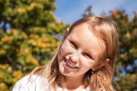 Foto de Niña sonriente alegre 8-9 años con aparato de ortodoncia, retrato de cerca de un niño en la naturaleza - Imagen libre de derechos