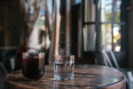 Glasses with tea and glass of water on wooden table, blurred backgroun, close view