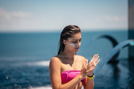Photo for Portrait photo of smiling woman is applying sunscreen on her face. - Royalty Free Image