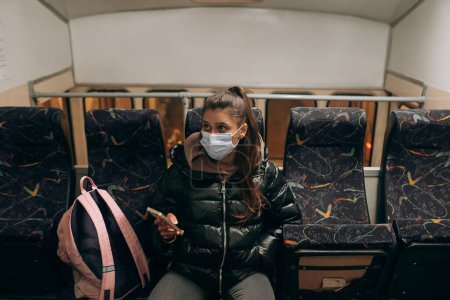Foto de Young woman with mask traveling in the public transport by bus. Unique protective mask of the respiratory tract from coronavirus. - Imagen libre de derechos