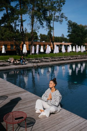 Téléchargez les photos : Jeune femme de fitness faisant sa routine de yoga matinale en plein air près de la piscine - en image libre de droit
