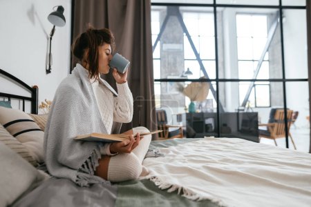 Téléchargez les photos : Belle livre de lecture femme et profiter du café chaud dans un appartement ensoleillé.Détente au lit. - en image libre de droit
