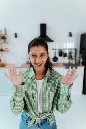 Foto de Mujer joven muestra sus manos en harina en la cocina a la cámara - Imagen libre de derechos