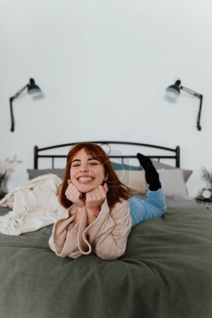 Téléchargez les photos : Joyeux jeune femme se couche sur le lit et regarde la caméra - en image libre de droit