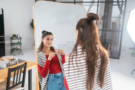 Happy young woman applies makeup on her face in front of the mirror