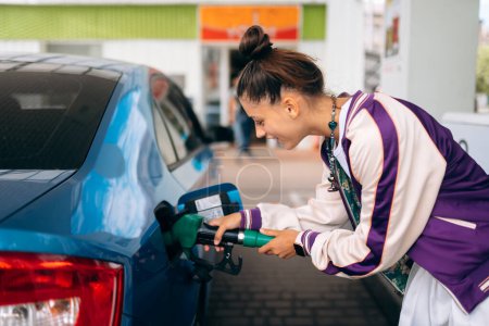 Téléchargez les photos : Cheerful young woman brunette filling her car with fuel at a gas station - en image libre de droit