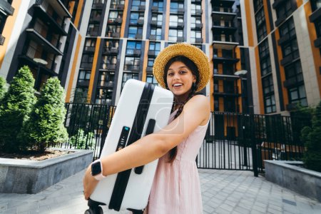 Foto de A young beautiful woman holds a suitcase in her hands in front of a modern house - Imagen libre de derechos