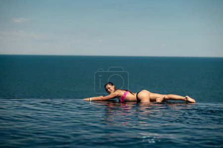 Téléchargez les photos : Happy woman in swimsuit swimming in infinity pool at luxury hotel against seafront. Relaxing, summer, travel, holiday, vacation and weekend concept - en image libre de droit