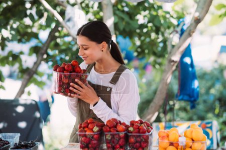 Téléchargez les photos : Young positive salesgirl at job, selling sells home-grown vegetables and fruits in vegetable shop - en image libre de droit