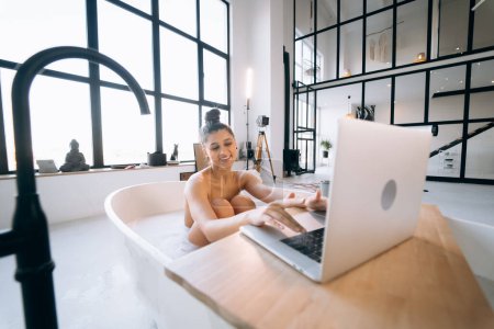 Photo for Young woman working on laptop while taking a bathtub at home - Royalty Free Image