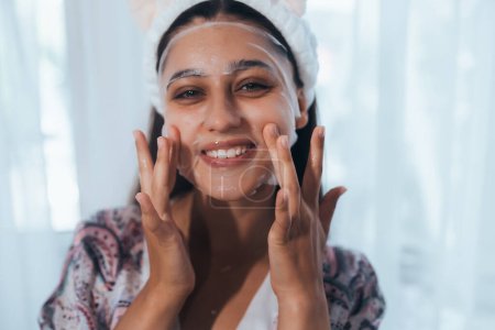 Téléchargez les photos : Jeune modèle appliquant un traitement cosmétique à la crème sur son visage - en image libre de droit