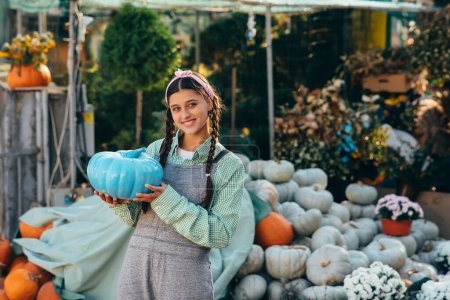 Photo for Happy female farmer holding blue colored pumpkin, decorated pumpkin for holiday. Halloween preparation concept. - Royalty Free Image