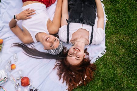 Foto de Two women having picnic together, laying on the plaid on the lawn - Imagen libre de derechos