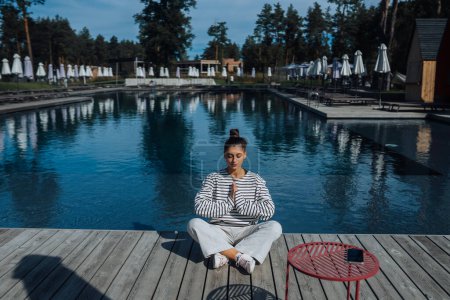 Téléchargez les photos : Jeune femme de fitness faisant sa routine de yoga matinale en plein air près de la piscine - en image libre de droit