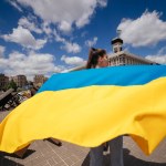 A young woman carries the flag of Ukraine fluttering behind her in the street