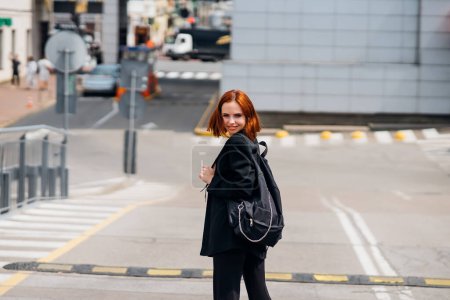 Téléchargez les photos : Jeune belle femme souriante heureuse avec sac à dos pose sur une caméra tout en se tenant sur la route - en image libre de droit