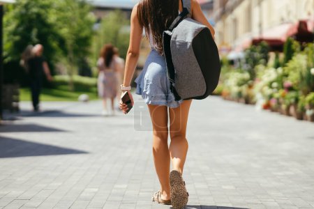 Urban young hipster woman with stylish backpack walks around the city near a building in the spring day. Pretty girl travels.