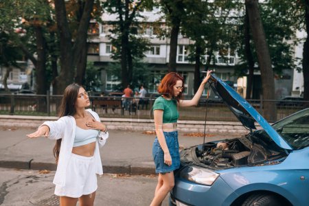 Téléchargez les photos : Deux femmes avec une voiture en panne sur la route chercher quelqu'un d'aide. - en image libre de droit