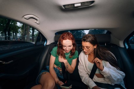 Foto de Vida real de amigos juntos en el asiento trasero de un taxi sosteniendo teléfonos celulares y revisando mensajes. - Imagen libre de derechos