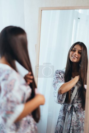 Photo for Woman combing hair in front of her mirror. - Royalty Free Image