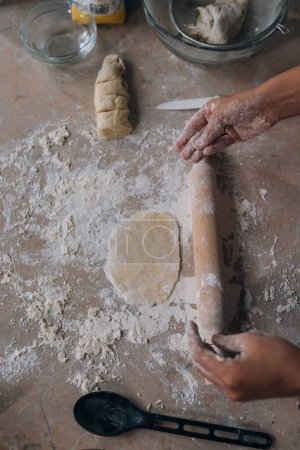 Foto de Primer plano de la mujer joven que rueda la masa con el rodillo para la panadería casera en la mesa - Imagen libre de derechos