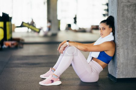 Healthy young female sitting relaxed after training in gym. Woman resting after workout at gym.