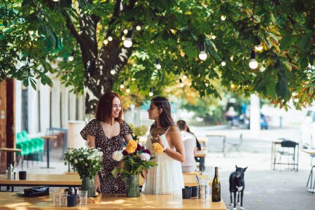 Photo for Two young women take orders and make up a beautiful festive bouquet. Floristry and making bouquets at the street caffe. Small business. - Royalty Free Image