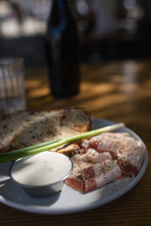 Photo for Close up view slices of smoked bacon meat with rye whole grain black bread, green onion and sour cream on the table. Selective focus, copy space. Country style organic food. - Royalty Free Image