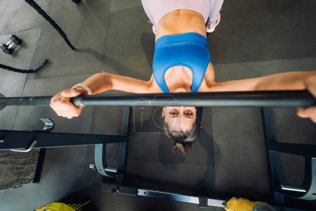 Téléchargez les photos : Belle femme faisant des exercices avec haltère sur un banc d'entraînement de presse dans un centre de fitness - en image libre de droit
