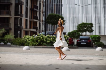 Téléchargez les photos : Jeune sexy belle jolie femme en robe blanche marchant dans la rue de la ville - en image libre de droit