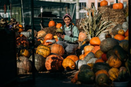 Photo for Happy farmer woman in a denim jumpsuit chooses ripe pumpkin, autumn harvest. Concept of agriculture. - Royalty Free Image
