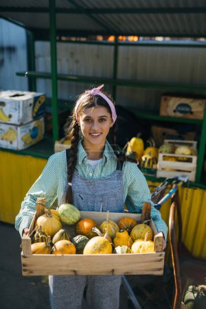 Photo for Farmer woman holds a wooden box with pumpkins in her hands. Concept of market. - Royalty Free Image