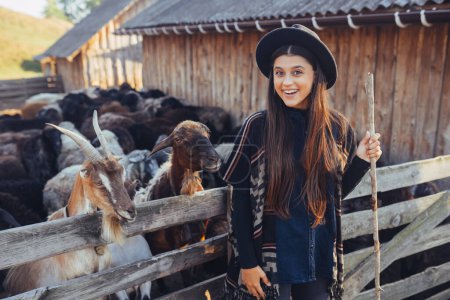 Foto de Una joven hermosa mujer cerca de una pluma con cabras posa para la cámara - Imagen libre de derechos