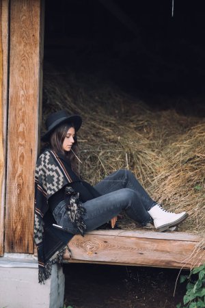 Téléchargez les photos : Jeune femme brune pose tout en étant assis à l'entrée de la grange. Style rural. - en image libre de droit