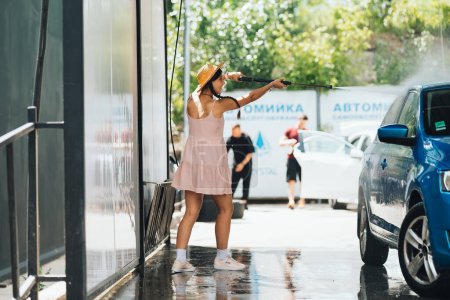 Téléchargez les photos : Brunette d'un tuyau haute pression lave la voiture lors d'un lavage de voiture - en image libre de droit