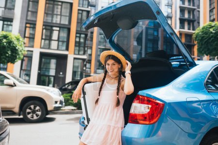 Téléchargez les photos : Jeune femme heureuse emballant sa valise dans la botte à bagages de la voiture. Concept de vacances. - en image libre de droit