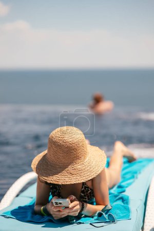 Téléchargez les photos : A young beautiful woman in swimsuit sunbathes on a sun lounger by the pool at the hotel.Summer concept. - en image libre de droit