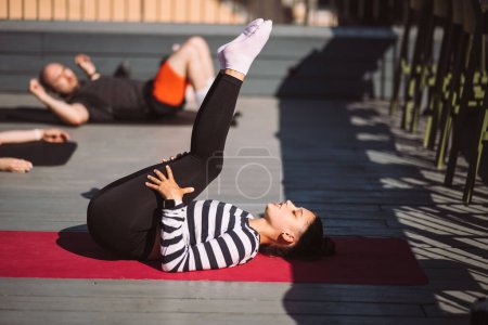 Foto de Yogi woman and diverse group of young sporty people practicing yoga, female students training at houses roof. Well being, wellness concept - Imagen libre de derechos