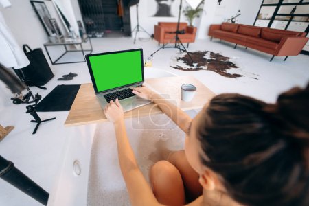 Téléchargez les photos : Jeune femme travaillant sur un ordinateur portable tout en prenant une baignoire à la maison - en image libre de droit