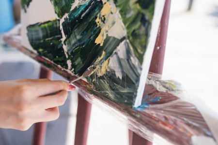 Téléchargez les photos : Gros plan d'une main de femme appliquant de la peinture sur une toile avec une spatule - en image libre de droit