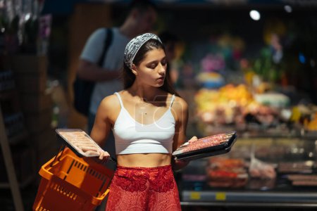 Foto de Mujer joven comprando carne en una tienda de comestibles - Imagen libre de derechos