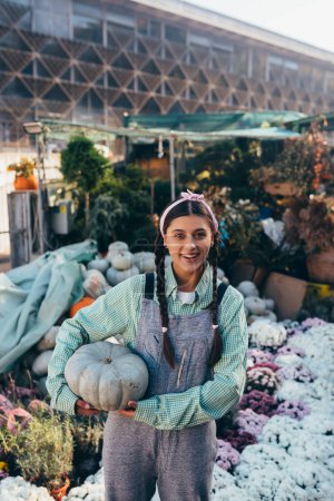Photo for Happy farmer woman in a denim jumpsuit holds ripe pumpkin, autumn harvest. Concept of agriculture. - Royalty Free Image