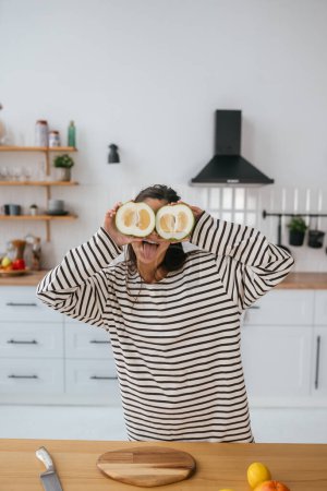 Téléchargez les photos : Femme tenir les fruits coupés au niveau des yeux au lieu de lunettes dans la cuisine - en image libre de droit