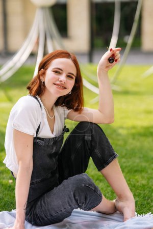 Téléchargez les photos : Joyeux jeune femme assise sur une couverture à la pelouse du parc. Vue rapprochée - en image libre de droit
